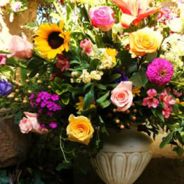 Mixed bouquet with roses, sunflowers, and lilies in a white urn vase