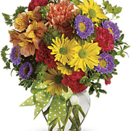 Mixed bouquet of colorful flowers in a glass vase with a polka-dot ribbon