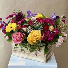 Mixed bouquet of roses, gerbera daisies, and purple blooms in a wooden box