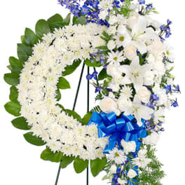 Standing wreath of white flowers with blue accents and a blue bow on an easel