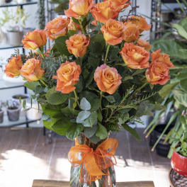 Orange roses in a clear glass vase with an orange ribbon