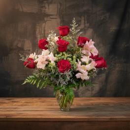 Red roses and pale pink flowers in a glass vase
