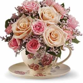 Pink and cream roses arranged in a floral teacup with saucer