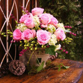 Pink roses arranged in a decorative vase with pinecones nearby