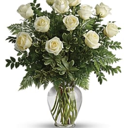 White roses arranged in a clear glass vase with greenery