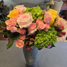 Pink and yellow roses with green hydrangeas in a tall vase