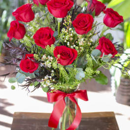 Red roses arranged in a glass vase with a red ribbon