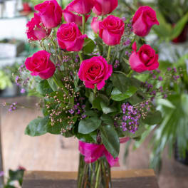 Pink roses arranged in a clear glass vase with small purple filler flowers.