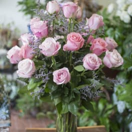 Pink roses arranged in a clear glass vase with purple filler flowers.