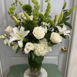 White lilies, roses, and green blooms arranged in a clear glass vase.
