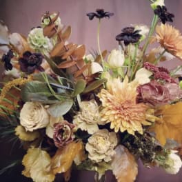 Mixed bouquet in a glass vase with peach, cream, and dark purple blooms