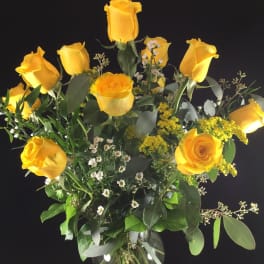 Yellow roses in a clear glass vase with mixed greenery