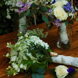 White and purple floral bouquets in glass jars on a wooden table