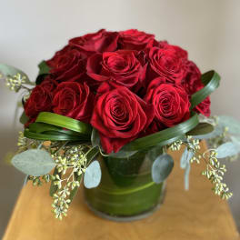 Red roses arranged in a green glass vase with eucalyptus accents