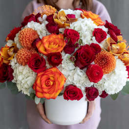 Large bouquet of red, orange, and white flowers in a white vase