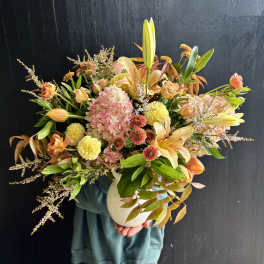 Mixed bouquet of peach and pink flowers in a white vase