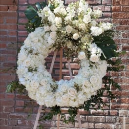 Large white floral wreath on a wooden easel against a brick wall