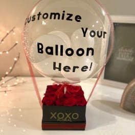 Clear balloon over a box of red roses with custom text