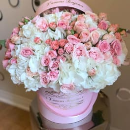 Round hatbox arrangement of pink roses and white flowers in a pink box.