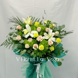 Bouquet of white lilies, pale roses, and green hydrangeas wrapped in teal paper