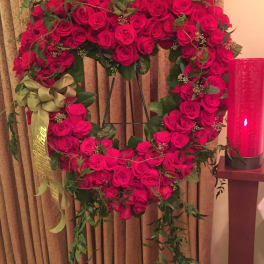 Heart-shaped wreath of red roses with a ribbon on a stand