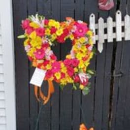 Heart-shaped floral wreath on a fence with bright pink, yellow, and orange flowers