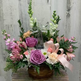 Basket arrangement with pink and purple flowers around a clear glass cross