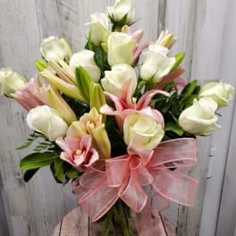Bouquet of white roses and pink lilies in a glass vase with a pink ribbon