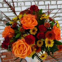 Bouquet of orange and red roses with yellow daisies in a white vase