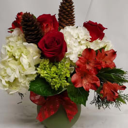 Red roses and white hydrangeas in a green vase with pinecones and a red ribbon