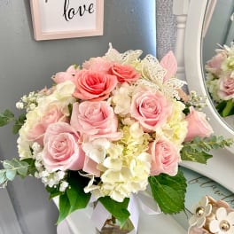 Pink roses and white hydrangeas arranged in a glass vase with a ribbon.