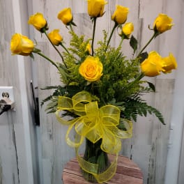 Yellow roses arranged in a clear glass vase with a yellow ribbon.