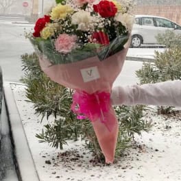 Handheld bouquet of red, pink, and white carnations wrapped in pink paper with a bow