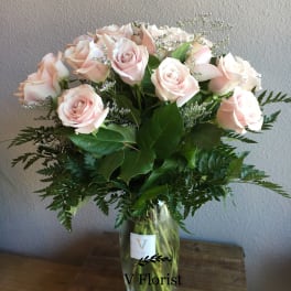 Tall vase arrangement of pale pink roses with white filler flowers.