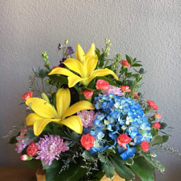 Basket arrangement with yellow lilies, blue hydrangeas, and pink flowers