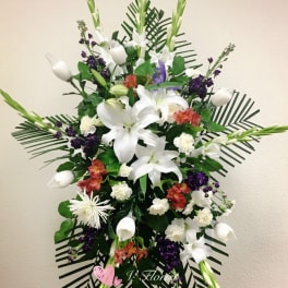 Tall funeral spray with white lilies, purple accents, and palm fronds