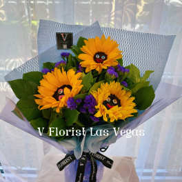 Hand-tied bouquet of yellow sunflowers with purple accents in blue wrap on a stand