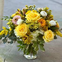 Yellow roses and mixed flowers arranged in a clear glass vase