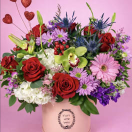 Mixed bouquet of red roses, pink daisies, and orchids in a pink hat box
