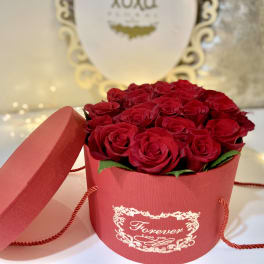 Red roses arranged in a round red gift box with a lid beside it.