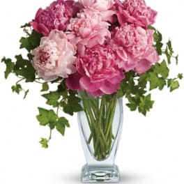 Pink peonies in a clear glass vase with trailing greenery