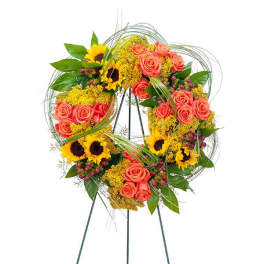 Standing wreath of orange roses and yellow sunflowers with decorative looping grasses