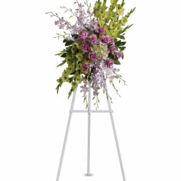 Tall floral spray with purple roses and green orchids on a white easel