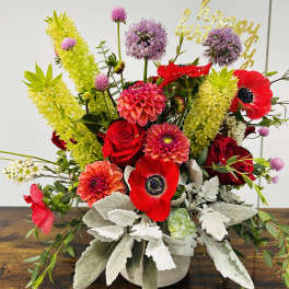 Bright mixed bouquet with red roses, pink dahlias, and purple blooms in a white vase