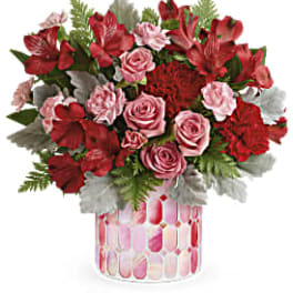 Red and pink flower bouquet in a patterned glass vase