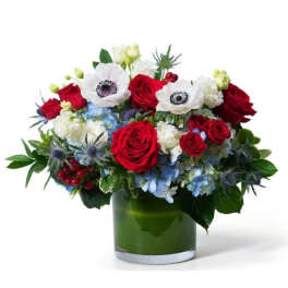 Red, white, and blue flower arrangement with roses and anemones in a green-lined glass cylinder vase