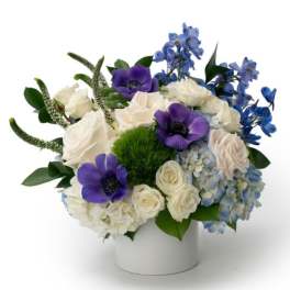 Low white vase of white roses, blue hydrangeas, and purple anemones