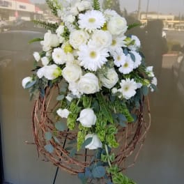 White floral standing arrangement with roses and daisies on a twig wreath stand