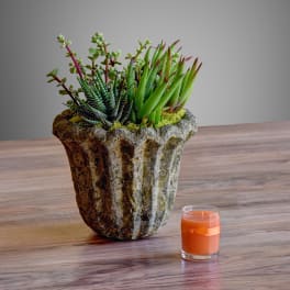 Succulent arrangement in a textured stone planter beside an orange candle