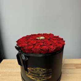 Round black hatbox filled with red roses and one gold rose on a wooden table